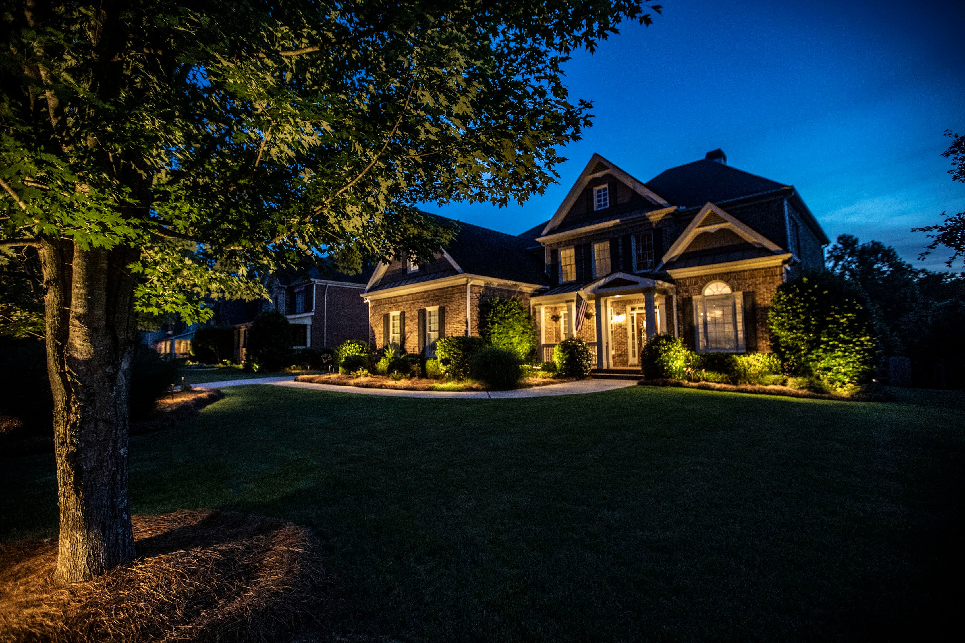 Twilight Comprehensive Lighting Design Stunning brick home at twilight with comprehensive landscape lighting including tree uplighting, pathway lights, and architectural lighting in Auburn Alabama
