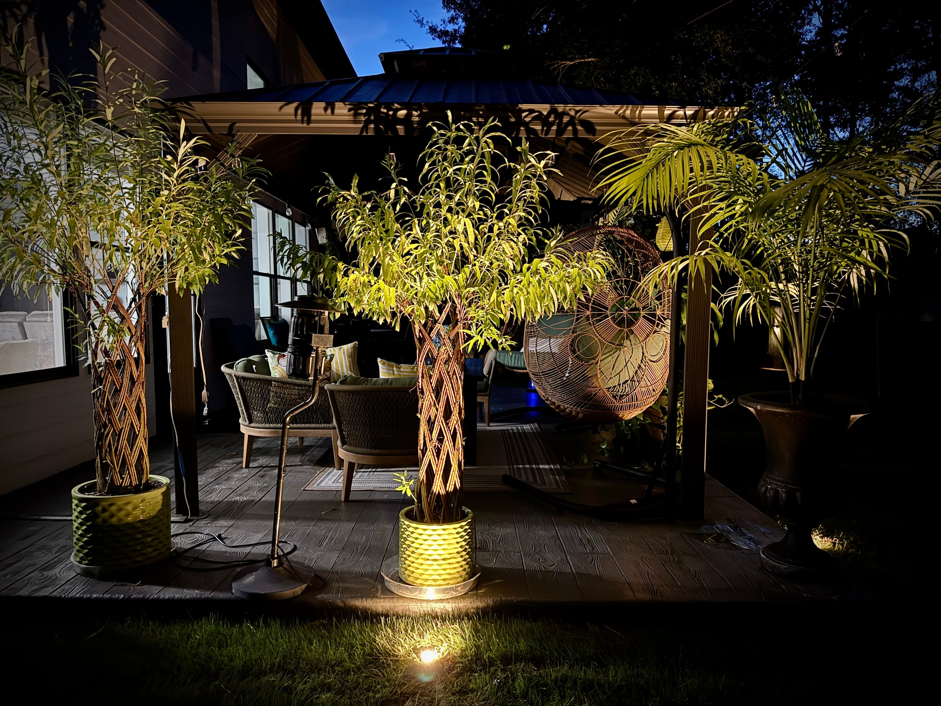 Luxury Outdoor Patio Lighting with Illuminated Planters Evening patio with uplighted palm planters, wicker furniture, and ambient outdoor lighting design