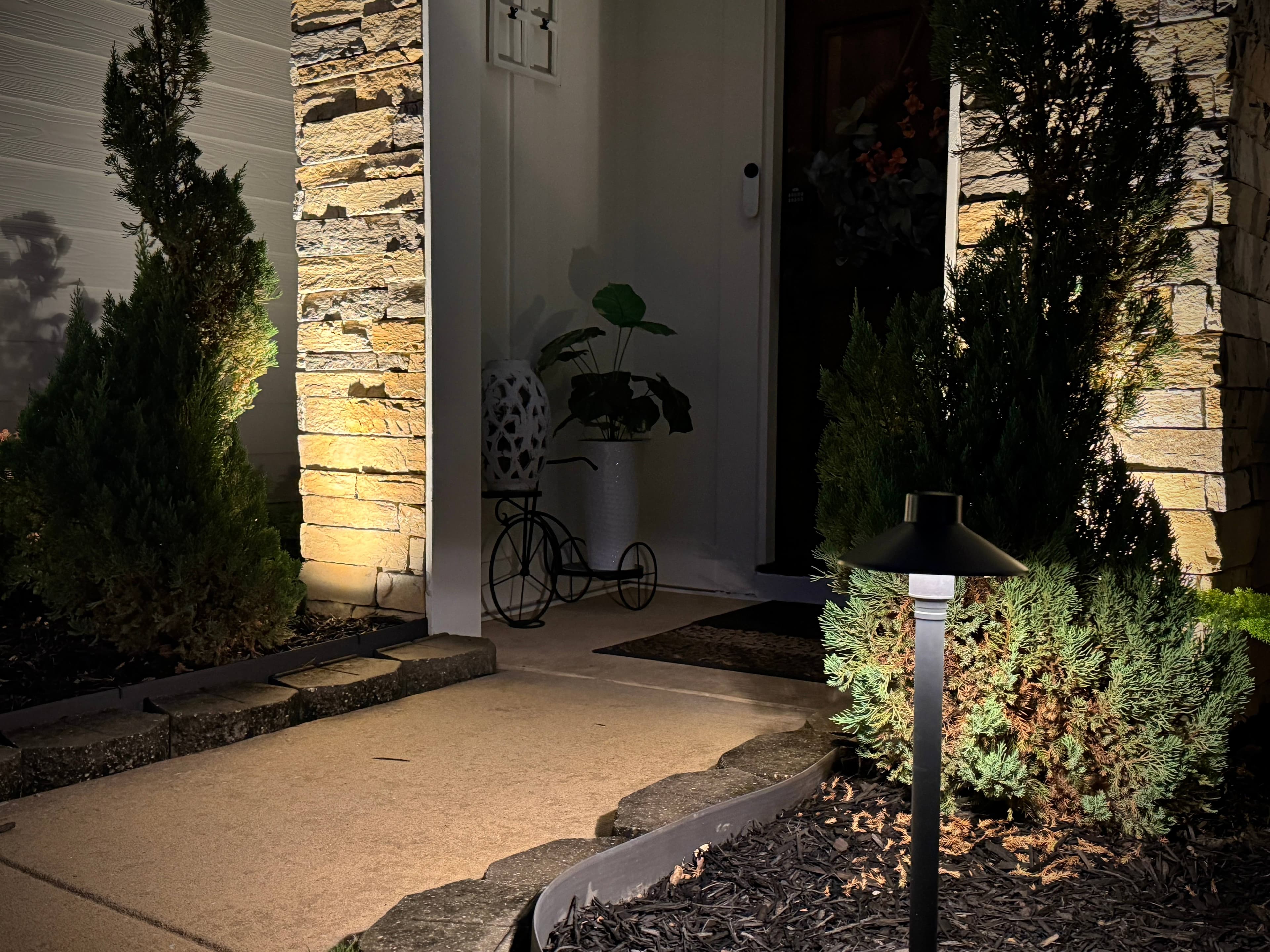 Residential Entrance Lighting with Stone Wall Uplighting Home entrance at night featuring illuminated stacked stone walls, pathway lighting, and landscape bed lights