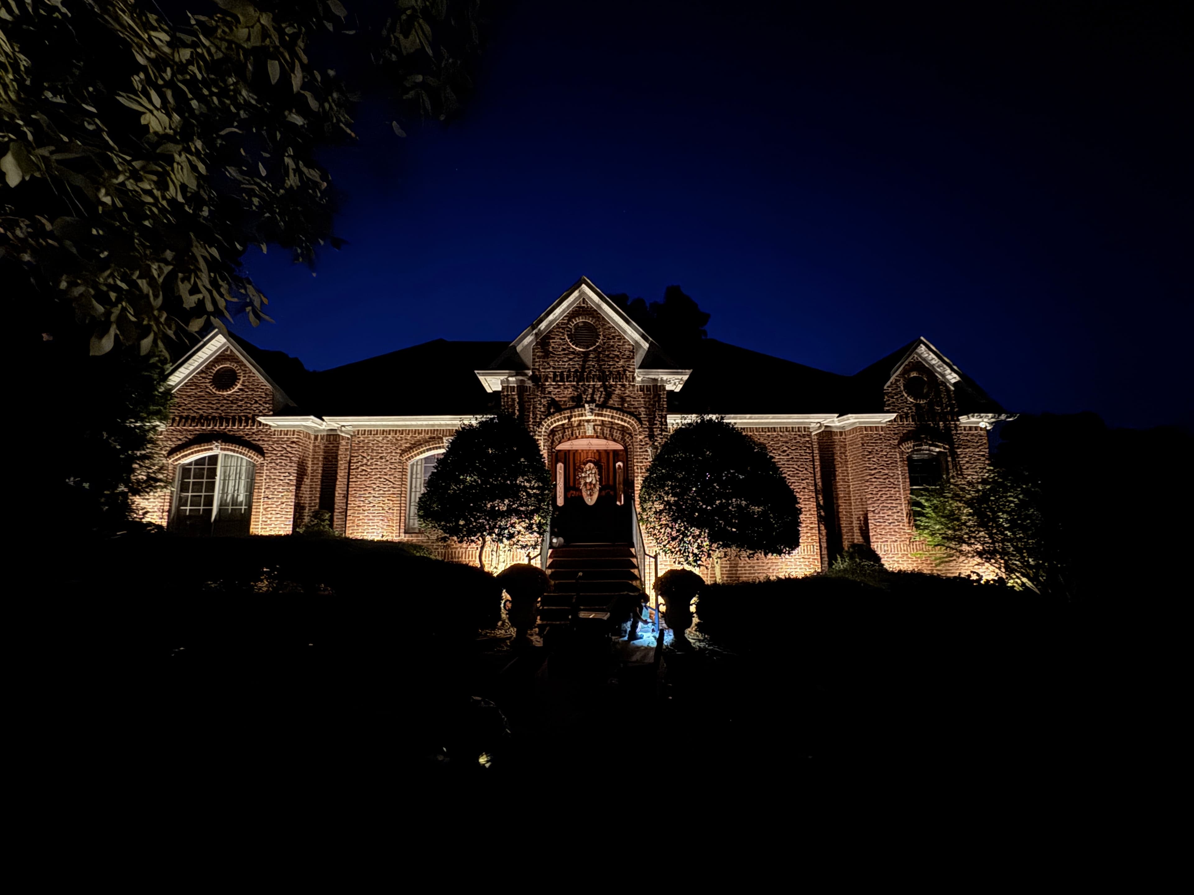 Brick Home Facade Architectural Lighting Traditional brick home exterior with dramatic uplighting on facade and architectural details at dusk