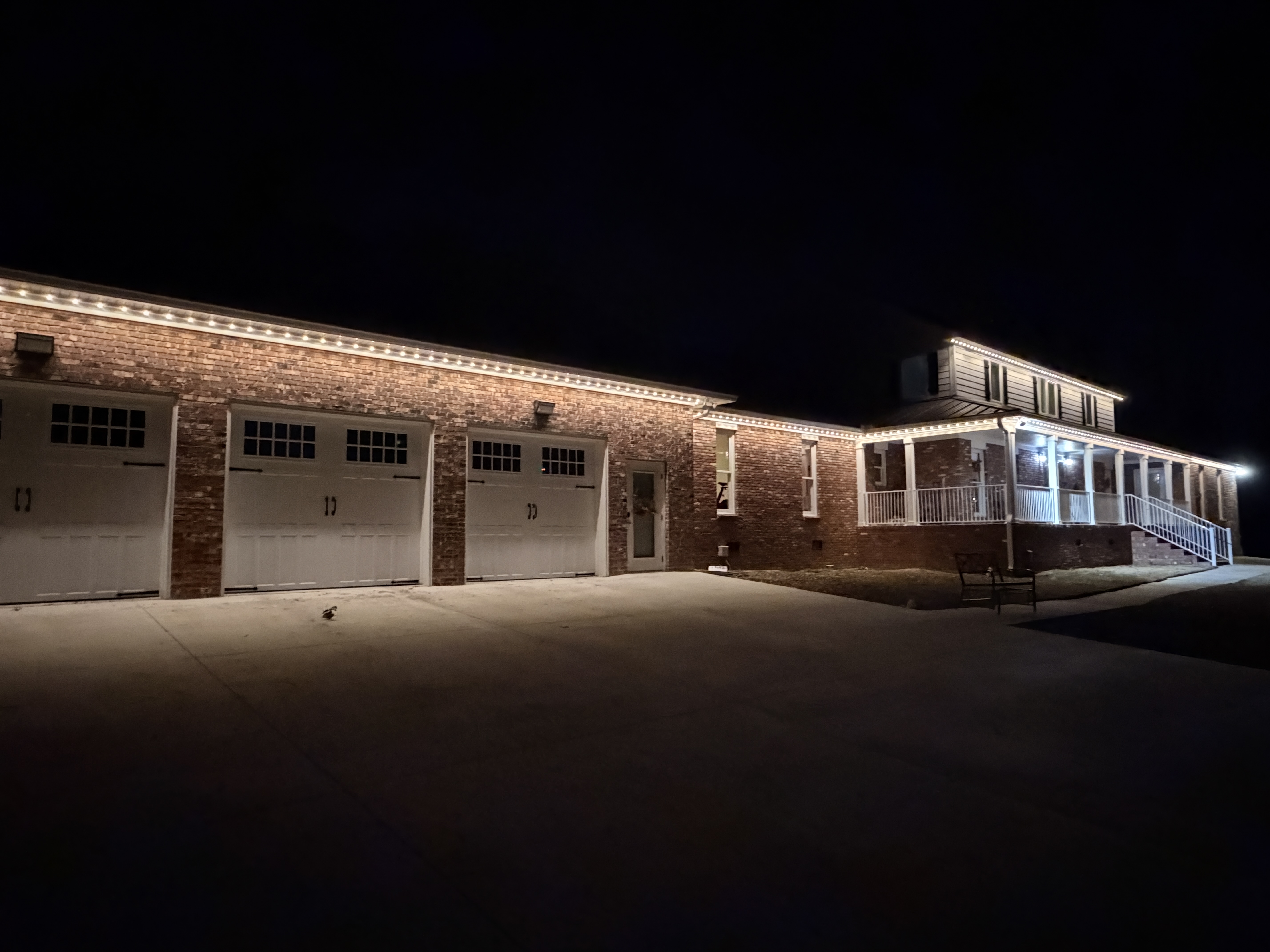 Warm white permanent lighting on brick home with wrap-around porch